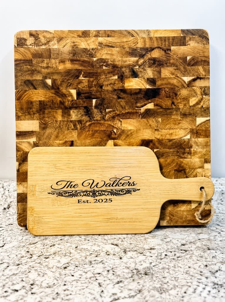 Laser-engraved bamboo serving board with The Walkers and Est 2025 beside an end-grain butcher block